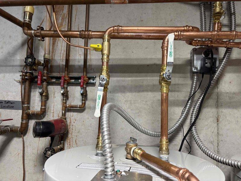 Installed two Bradford White electric water heaters in tandem configuration in utility room. Established complete copper piping network with manifold system featuring three-zone distribution valves for efficient hot water delivery throughout the residence. Connected units to existing water softener system using flexible stainless steel connectors and installed all required shut-off valves, pressure relief components, and electrical connections per manufacturer specifications and local code requirements.