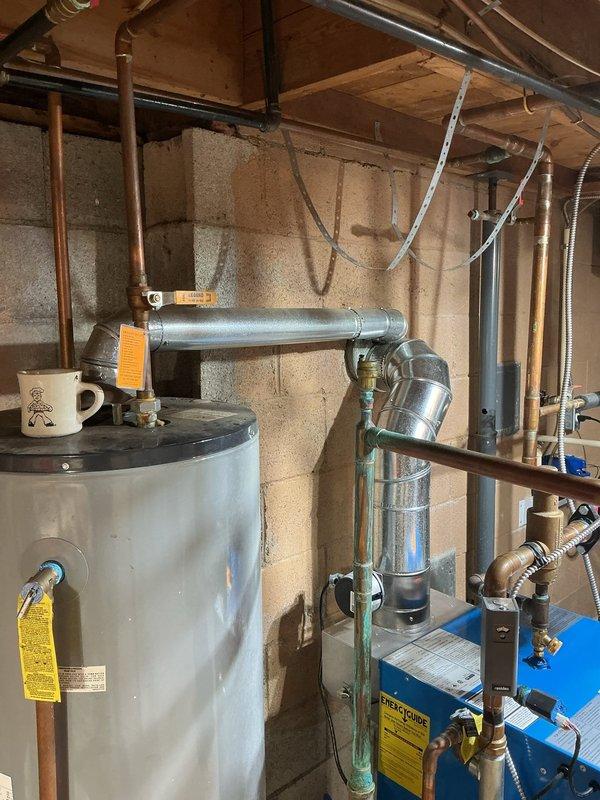 Conducted on-site evaluation of existing 50-gallon gas water heater located in basement mechanical room. Unit is estimated to be 10-15 years old based on visual inspection and shows typical signs of age-related wear. Photographed current installation including all water heater connections, copper supply and discharge piping, galvanized venting system, gas line configuration, and associated plumbing components. Documented existing setup showing standard residential installation with visible safety labels, temperature and pressure relief valve piping, and blue expansion tank mounted to the system. Prepared comprehensive estimate for replacement water heater installation to provide customer with options for upgrading aging equipment.