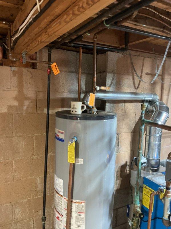 Conducted on-site evaluation of existing 50-gallon gas water heater located in basement mechanical room. Unit is estimated to be 10-15 years old based on visual inspection and shows typical signs of age-related wear. Photographed current installation including all water heater connections, copper supply and discharge piping, galvanized venting system, gas line configuration, and associated plumbing components. Documented existing setup showing standard residential installation with visible safety labels, temperature and pressure relief valve piping, and blue expansion tank mounted to the system. Prepared comprehensive estimate for replacement water heater installation to provide customer with options for upgrading aging equipment.