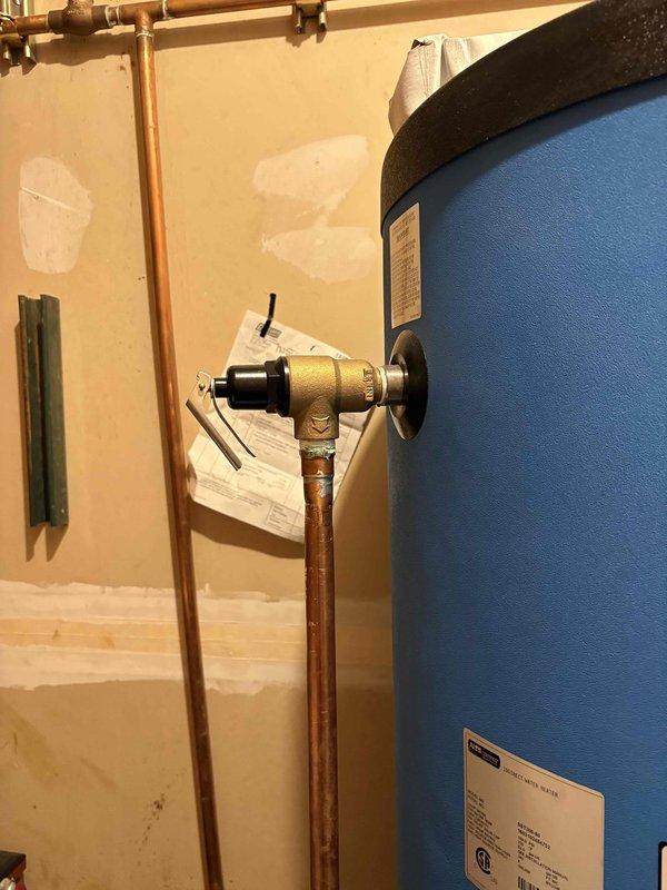 Responded to water leak call and conducted diagnostic inspection. Upon arrival, identified source of leak as corroded temperature and pressure relief valve discharge pipe on water heater. Observed significant turquoise-green copper corrosion at pipe terminus with evidence of water damage on floor surface beneath. Documented conditions with photos showing advanced oxidation of copper piping and brownish residue staining on utility room floor. Advised homeowner of findings and recommended replacement of corroded discharge piping to prevent continued leakage.