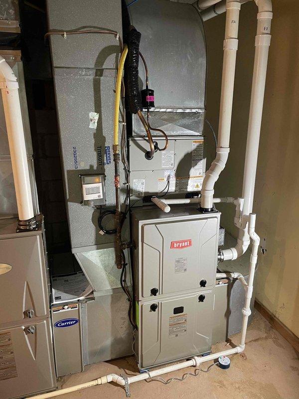 Completed full HVAC system replacement including outdoor condenser unit and indoor air handler. Installed new cylindrical condenser with vertical grille fins on existing concrete pad adjacent to residence, ensuring proper clearance and positioning. Replaced indoor components including Bryant furnace and Carrier air handler unit in utility room, establishing complete heating and cooling system integration. Configured all electrical connections, refrigerant lines, and condensate drainage using PVC piping. Verified proper ductwork connections to metal plenum system and ensured all flexible duct transitions were secure. System tested and confirmed operational with all safety controls functioning correctly.
