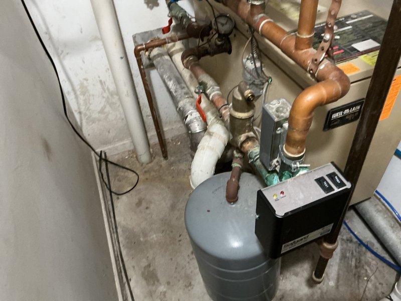 Completed on-site evaluation of existing Weil-McLain boiler system and associated hydronic heating components in residential mechanical room. Documented current installation including water heater, expansion tank, multiple zone circulation pumps with individual controls, complex copper piping network with various shut-off valves, and flexible connector hoses. Photographed system configuration showing aged piping with mineral deposits, electrical connections, PVC venting, and multi-zone manifold setup with red circulation pumps and ball valves for zone isolation. Provided comprehensive estimate for boiler replacement and system upgrades based on assessment of existing equipment condition and installation requirements.