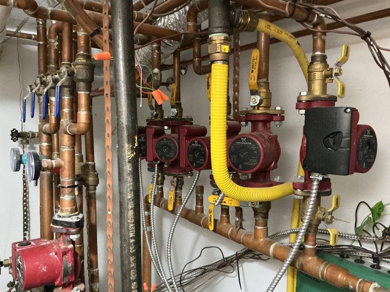Completed on-site evaluation of existing Weil-McLain boiler system and associated hydronic heating components in residential mechanical room. Documented current installation including water heater, expansion tank, multiple zone circulation pumps with individual controls, complex copper piping network with various shut-off valves, and flexible connector hoses. Photographed system configuration showing aged piping with mineral deposits, electrical connections, PVC venting, and multi-zone manifold setup with red circulation pumps and ball valves for zone isolation. Provided comprehensive estimate for boiler replacement and system upgrades based on assessment of existing equipment condition and installation requirements.