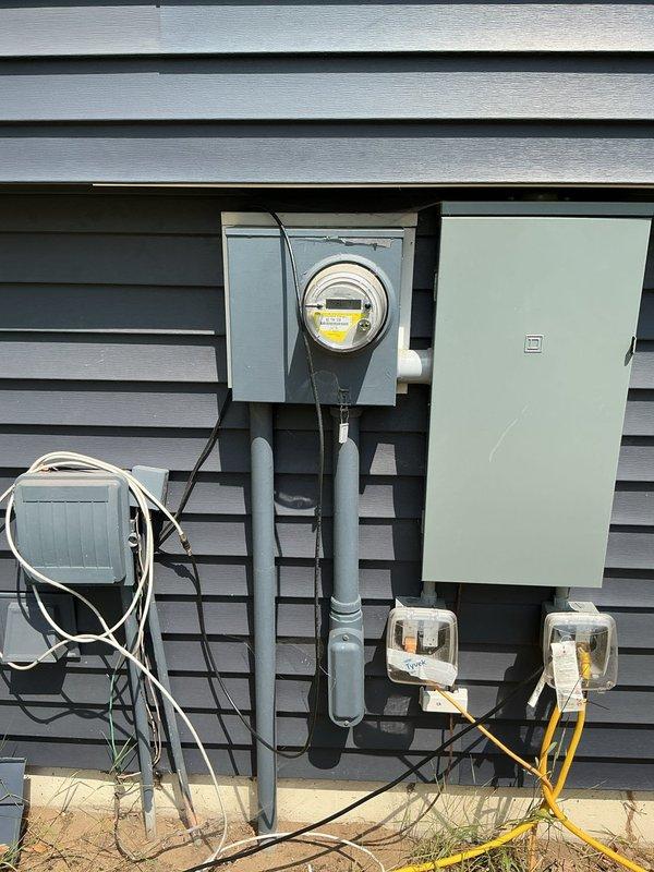 Conducted sales consultation for standby generator installation at residential property currently undergoing post-fire reconstruction. Documented existing electrical service entrance with meter enclosure, main disconnect panel, and PVC conduit routing, along with exterior receptacles and communication wiring. Photographed natural gas meter installation with supply piping to assess utility infrastructure availability for generator fuel source. Evaluated electrical panel capacity and gas service configuration to determine appropriate generator sizing and installation requirements for whole-home backup power system.