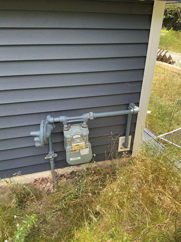 Conducted sales consultation for standby generator installation at residential property currently undergoing post-fire reconstruction. Documented existing electrical service entrance with meter enclosure, main disconnect panel, and PVC conduit routing, along with exterior receptacles and communication wiring. Photographed natural gas meter installation with supply piping to assess utility infrastructure availability for generator fuel source. Evaluated electrical panel capacity and gas service configuration to determine appropriate generator sizing and installation requirements for whole-home backup power system.
