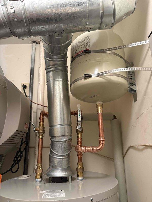 Returned to installation site to complete water heater system modifications. Installed support bracket for expansion tank to ensure proper mounting and code compliance. Performed repiping work on copper supply lines, including new brass fittings and shut-off valves to improve system configuration and accessibility. Secured dual expansion tanks with metal hose clamps and verified all connections for proper operation. Total work time approximately three hours. Documentation photos captured showing completed installation with properly supported expansion tanks, updated copper piping connections, and water heater assembly in utility closet.