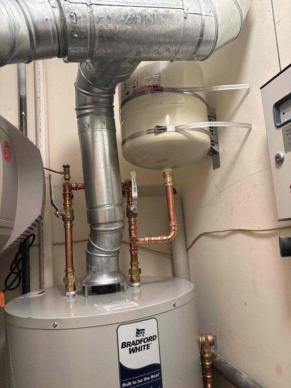 Returned to installation site to complete water heater system modifications. Installed support bracket for expansion tank to ensure proper mounting and code compliance. Performed repiping work on copper supply lines, including new brass fittings and shut-off valves to improve system configuration and accessibility. Secured dual expansion tanks with metal hose clamps and verified all connections for proper operation. Total work time approximately three hours. Documentation photos captured showing completed installation with properly supported expansion tanks, updated copper piping connections, and water heater assembly in utility closet.