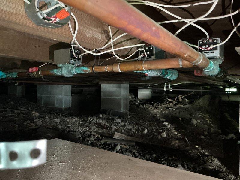 Conducted on-site assessment for replacement of 30-year-old heating system. Upon inspection, identified existing equipment as a Weil-McLain Gold boiler unit showing significant age-related wear, dust accumulation, and surface discoloration. Evaluated copper supply and return piping displaying oxidation and patina consistent with system age. Documented current installation configuration including piping connections, electrical routing, and equipment placement in basement utility area. Assessed crawl space conditions revealing aged copper distribution lines with corrosion, electrical wiring runs along floor joists, and concrete block foundation supports. Captured photographic documentation of existing boiler unit, associated plumbing connections, and underfloor distribution system for replacement planning purposes. Provided comprehensive evaluation for complete heating system replacement estimate.
