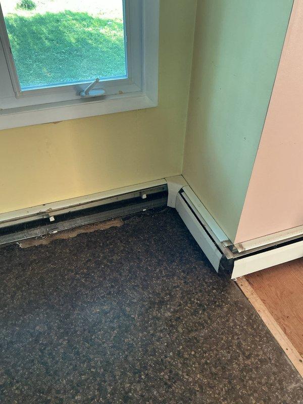 Consulted with contractor regarding baseboard kick plate installation in multi-room residential space. Documented existing baseboard heating units along yellow and mint green painted walls, noting heater cover requiring proper securing and assessing transition areas between carpeted and hardwood flooring for kick plate installation specifications.