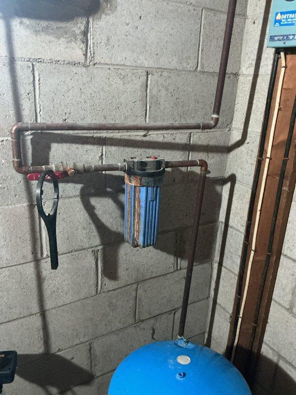 Performed water sample collection from residential water filtration and treatment system. System includes whole-house filtration unit with clear blue housing, pressure tank, and water softening equipment with digital control unit. Documented existing plumbing configuration and equipment condition with photographs for reference.