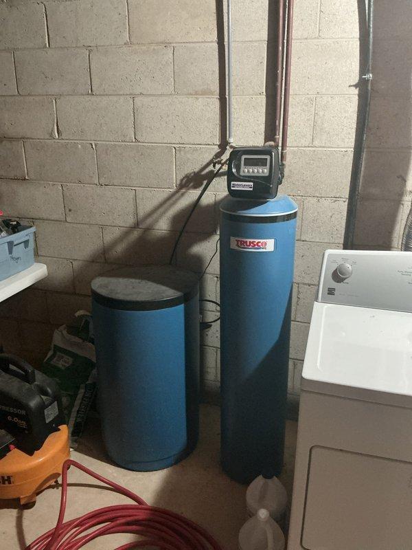 Performed water sample collection from residential water filtration and treatment system. System includes whole-house filtration unit with clear blue housing, pressure tank, and water softening equipment with digital control unit. Documented existing plumbing configuration and equipment condition with photographs for reference.