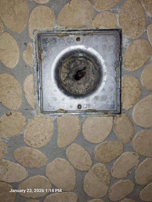 Inspected shower drain system in pebble-tile bathroom floor due to reported drainage issues. Documented condition of square metal drain plate showing significant wear and discoloration. After service, confirmed proper drain function with water flowing freely through the brass/copper drain assembly. Inspected shower drain system in pebble-tile bathroom floor due to reported drainage issues. Documented condition of square metal drain plate showing significant wear and discoloration. After service, confirmed proper drain function with water flowing freely through the brass/copper drain assembly.
