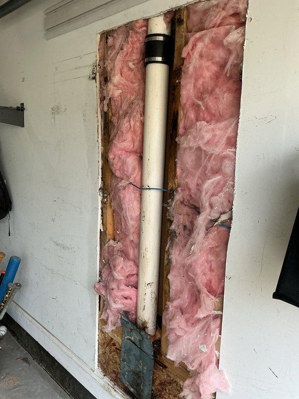 Chamblee, GA - Conducted follow-up inspection regarding customer's reported leak in garage. Accessed wall cavity by opening drywall, revealing PVC pipe with black coupling running vertically through wooden studs. Observed pink fiberglass insulation surrounding the pipe, with signs of compression/disturbance where insulation meets pipe, potentially indicating the source of the leak. Chamblee, GA - Conducted follow-up inspection regarding customer's reported leak in garage. Accessed wall cavity by opening drywall, revealing PVC pipe with black coupling running vertically through wooden studs. Observed pink fiberglass insulation surrounding the pipe, with signs of compression/disturbance where insulation meets pipe, potentially indicating the source of the leak.