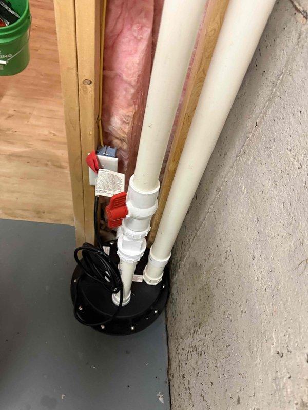 Installed special order pump system in basement utility area, including vertical PVC piping with shut-off valves against concrete wall. Setup includes proper electrical connections to the circular pump unit positioned at the base of the drainage system adjacent to exposed framing with fiberglass insulation. Installed special order pump system in basement utility area, including vertical PVC piping with shut-off valves against concrete wall. Setup includes proper electrical connections to the circular pump unit positioned at the base of the drainage system adjacent to exposed framing with fiberglass insulation.