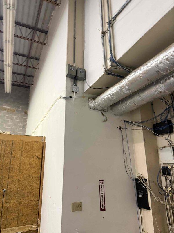 Inspected exterior brick wall water spigot fixture and interior commercial utility room. Documented condition of wall-mounted water connection point with metallic base plate and examined interior mechanical space containing exposed ductwork, electrical conduits, junction boxes, and service panel for approved quote specifications. Inspected exterior brick wall water spigot fixture and interior commercial utility room. Documented condition of wall-mounted water connection point with metallic base plate and examined interior mechanical space containing exposed ductwork, electrical conduits, junction boxes, and service panel for approved quote specifications.