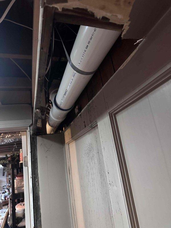 Inspected HVAC ductwork connection showing condensation issues at metal elbow joint secured with green-gasketed clamps. Examined exposed PVC plumbing pipe installation in ceiling/wall cavity with visible structural elements including damaged drywall and wood framing. Inspected HVAC ductwork connection showing condensation issues at metal elbow joint secured with green-gasketed clamps. Examined exposed PVC plumbing pipe installation in ceiling/wall cavity with visible structural elements including damaged drywall and wood framing.