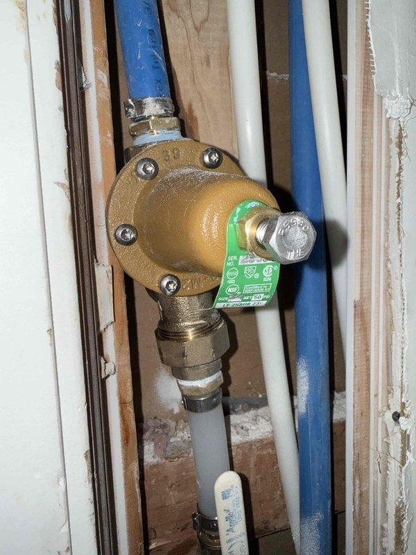 Installed new pressure regulating valve (PRV) in customer's water supply system, connecting to existing PEX and PVC piping within the wall cavity. Accessed plumbing through wall opening, replaced failed valve component with proper fittings and ensured secure connections to prevent leaks.
