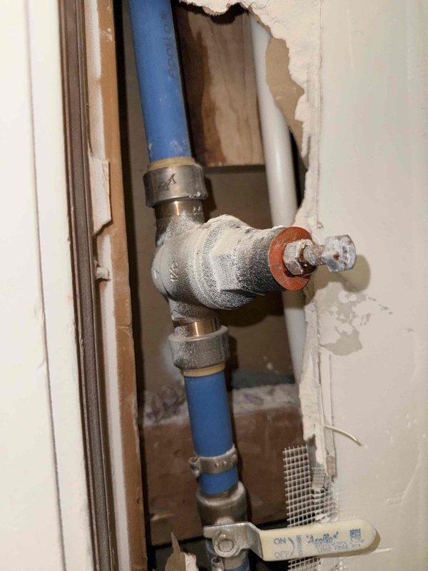 Installed new pressure regulating valve (PRV) in customer's water supply system, connecting to existing PEX and PVC piping within the wall cavity. Accessed plumbing through wall opening, replaced failed valve component with proper fittings and ensured secure connections to prevent leaks.