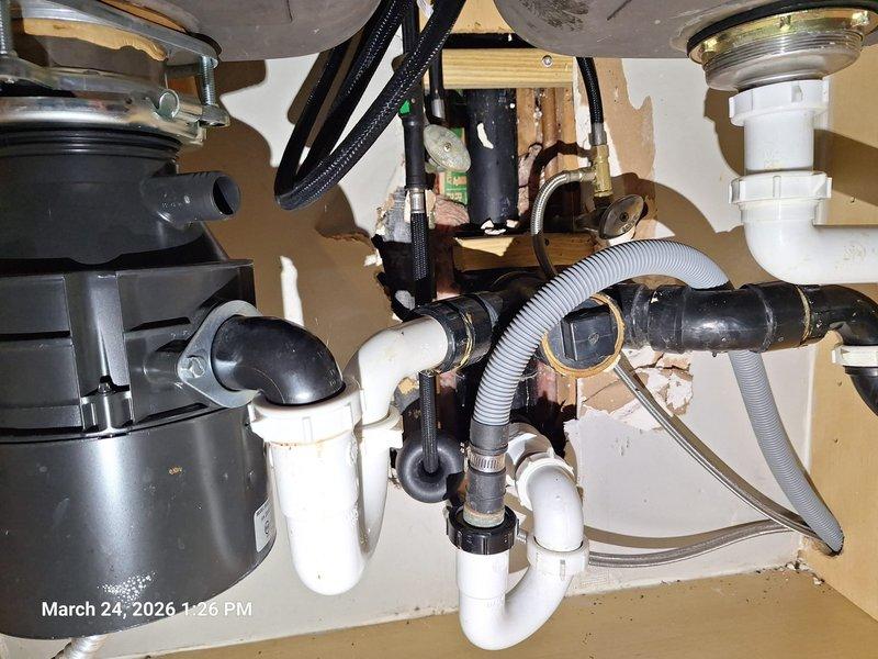 Responded to kitchen sink leak reported beneath the basin. Upon inspection, discovered water infiltration had caused significant deterioration to the wall cavity behind the sink, with extensive moisture damage to drywall and visible staining on interior framing. Assessed the complete under-sink plumbing assembly, including double-basin configuration with garbage disposal unit, PVC drain lines, P-traps, and dishwasher connection. Tightened loose faucet mounting hardware and supply line connections that were causing the drip beneath the sink. Verified proper sealing of all drain connections and inspected hose clamps on flexible lines for secure attachment. Tested faucet operation and checked all plumbing connections for leaks after repairs were completed. Responded to kitchen sink leak reported beneath the basin. Upon inspection, discovered water infiltration had caused significant deterioration to the wall cavity behind the sink, with extensive moisture damage to drywall and visible staining on interior framing. Assessed the complete under-sink plumbing assembly, including double-basin configuration with garbage disposal unit, PVC drain lines, P-traps, and dishwasher connection. Tightened loose faucet mounting hardware and supply line connections that were causing the drip beneath the sink. Verified proper sealing of all drain connections and inspected hose clamps on flexible lines for secure attachment. Tested faucet operation and checked all plumbing connections for leaks after repairs were completed.