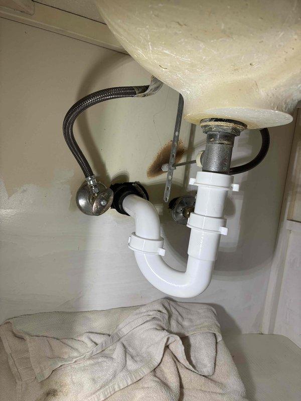 Responded to service call for leak under bathroom vanity. Upon inspection, identified water damage evidenced by brownish staining on cabinet interior wall behind P-trap assembly. Assessed condition of existing white PVC drain assembly and chrome strainer, examined braided stainless steel supply lines and connections for source of leak. Documented plumbing configuration and moisture damage with photographs. Additionally provided estimate for garbage disposal installation as requested. Responded to service call for leak under bathroom vanity. Upon inspection, identified water damage evidenced by brownish staining on cabinet interior wall behind P-trap assembly. Assessed condition of existing white PVC drain assembly and chrome strainer, examined braided stainless steel supply lines and connections for source of leak. Documented plumbing configuration and moisture damage with photographs. Additionally provided estimate for garbage disposal installation as requested.