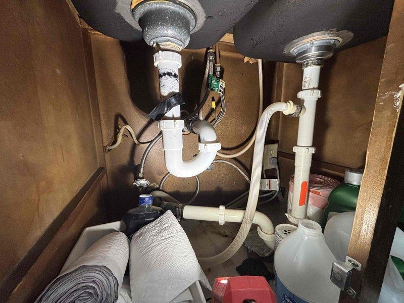 Responded to service call for leak under bathroom vanity. Upon inspection, identified water damage evidenced by brownish staining on cabinet interior wall behind P-trap assembly. Assessed condition of existing white PVC drain assembly and chrome strainer, examined braided stainless steel supply lines and connections for source of leak. Documented plumbing configuration and moisture damage with photographs. Additionally provided estimate for garbage disposal installation as requested. Responded to service call for leak under bathroom vanity. Upon inspection, identified water damage evidenced by brownish staining on cabinet interior wall behind P-trap assembly. Assessed condition of existing white PVC drain assembly and chrome strainer, examined braided stainless steel supply lines and connections for source of leak. Documented plumbing configuration and moisture damage with photographs. Additionally provided estimate for garbage disposal installation as requested.