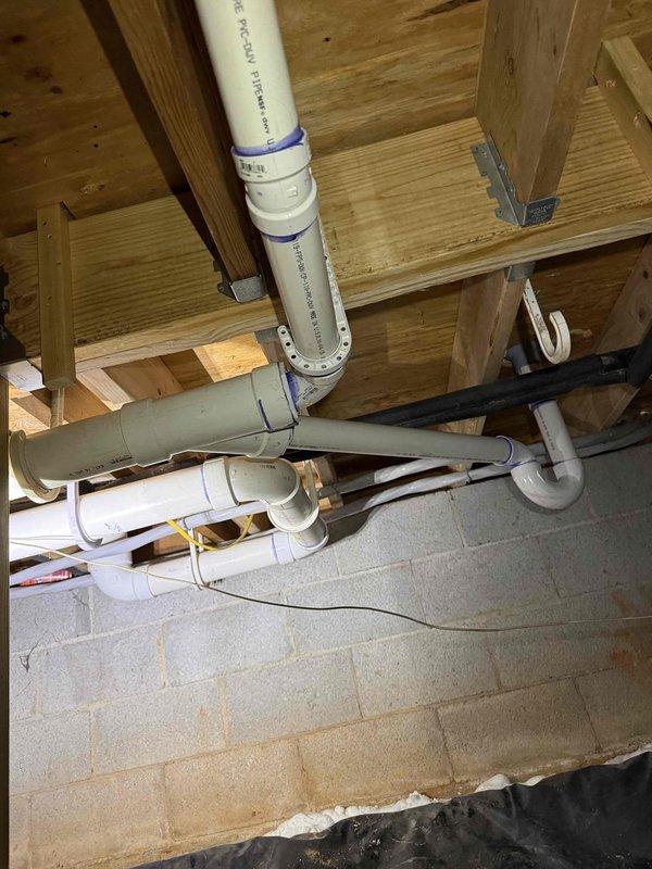 Completed bathroom drain repipe installation in crawl space and attic areas. Removed existing deteriorated drain lines and installed new white PVC drainage system with proper venting throughout the affected zones. Routed multiple drain lines through wooden framing members, securing pipes according to code requirements with appropriate hangers and supports. Installed various fittings including elbows, tees, and connectors to create functional drainage network. Applied primer and solvent cement to all PVC connections to ensure watertight, permanent joints. Coordinated pipe runs with existing structural elements including floor joists, studs, and foundation walls. Added black foam insulation to designated pipe sections for condensation control and noise reduction. Verified proper slope on all horizontal drain runs to ensure adequate drainage flow. System tested and confirmed operational with no leaks detected at any connection points. Completed bathroom drain repipe installation in crawl space and attic areas. Removed existing deteriorated drain lines and installed new white PVC drainage system with proper venting throughout the affected zones. Routed multiple drain lines through wooden framing members, securing pipes according to code requirements with appropriate hangers and supports. Installed various fittings including elbows, tees, and connectors to create functional drainage network. Applied primer and solvent cement to all PVC connections to ensure watertight, permanent joints. Coordinated pipe runs with existing structural elements including floor joists, studs, and foundation walls. Added black foam insulation to designated pipe sections for condensation control and noise reduction. Verified proper slope on all horizontal drain runs to ensure adequate drainage flow. System tested and confirmed operational with no leaks detected at any connection points.