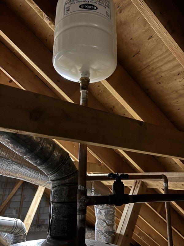 Responded to report of leak in ceiling. Upon inspection, located source in attic space where plumbing system components were installed. Examined water expansion tank mounted between wooden joists and associated piping connections. Identified leak originating from valve assembly and pipe fittings below expansion tank. Inspected pressure gauge on system which indicated proper pressure readings near zero. Checked all threaded brass connections and mounting points for signs of water intrusion. Tightened loose fittings and verified all connections were secure. Monitored system for additional leaks and confirmed repair was successful with no further water discharge detected. Responded to report of leak in ceiling. Upon inspection, located source in attic space where plumbing system components were installed. Examined water expansion tank mounted between wooden joists and associated piping connections. Identified leak originating from valve assembly and pipe fittings below expansion tank. Inspected pressure gauge on system which indicated proper pressure readings near zero. Checked all threaded brass connections and mounting points for signs of water intrusion. Tightened loose fittings and verified all connections were secure. Monitored system for additional leaks and confirmed repair was successful with no further water discharge detected.