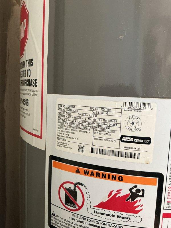 Responded to service call for water heater leaking at base. Upon inspection, found significant corrosion and rust damage to the water heater tank and surrounding support structure. The unit, manufactured in October 2017, exhibited deterioration at the base with visible moisture damage extending to the wooden support beam beneath the appliance. Documented equipment condition with photographs showing specification labels, safety warnings, and extent of corrosion damage affecting both the tank and mounting platform. The pressure relief valve assembly and associated brass fittings were inspected and photographed. Concrete floor showed evidence of water exposure from the leak. Customer was advised of findings and provided with photographic documentation of the water heater's condition for review and determination of next steps for repair or replacement. Responded to service call for water heater leaking at base. Upon inspection, found significant corrosion and rust damage to the water heater tank and surrounding support structure. The unit, manufactured in October 2017, exhibited deterioration at the base with visible moisture damage extending to the wooden support beam beneath the appliance. Documented equipment condition with photographs showing specification labels, safety warnings, and extent of corrosion damage affecting both the tank and mounting platform. The pressure relief valve assembly and associated brass fittings were inspected and photographed. Concrete floor showed evidence of water exposure from the leak. Customer was advised of findings and provided with photographic documentation of the water heater's condition for review and determination of next steps for repair or replacement.