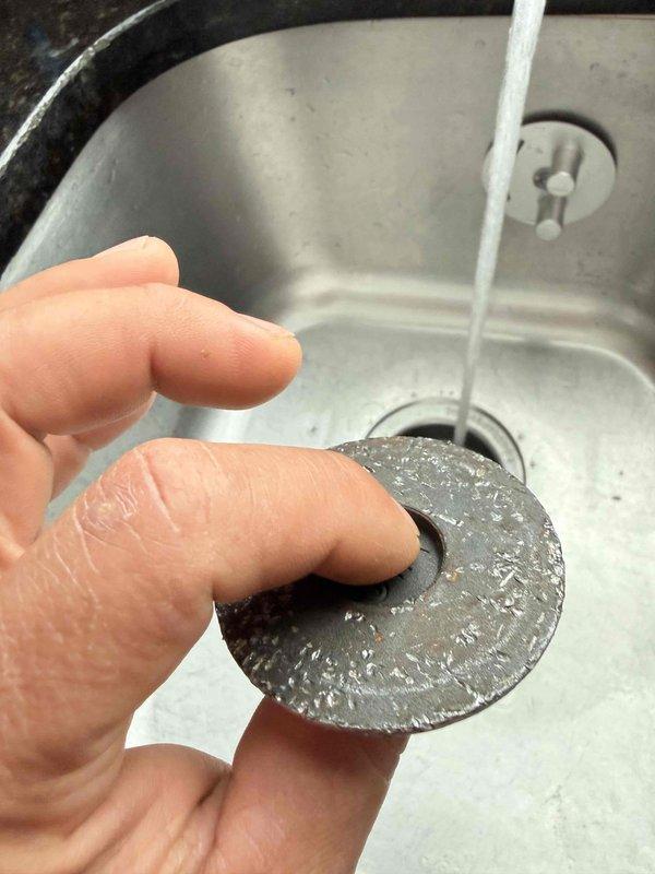 Responded to service call for non-functioning garbage disposal and continuously running toilet. Inspected kitchen sink drain system and removed heavily corroded disposal stopper and drain cover components showing significant mineral buildup from hard water exposure. Documented existing conditions with photographs showing extent of corrosion and component deterioration. Assessed garbage disposal unit for operational issues and identified failed internal mechanisms requiring replacement parts or unit replacement.