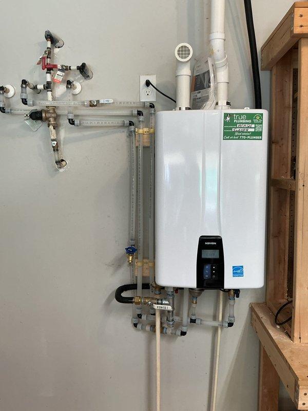 Completed installation of Navien tankless water heater system with full plumbing integration. Mounted unit to interior wall with proper venting using PVC exhaust piping, installed comprehensive valve manifold assembly with pressure gauges and isolation valves, and connected all hot and cold water supply lines using combination of copper, PEX, and flexible connectors with blue-handled shutoff valves for system control. Completed installation of Navien tankless water heater system with full plumbing integration. Mounted unit to interior wall with proper venting using PVC exhaust piping, installed comprehensive valve manifold assembly with pressure gauges and isolation valves, and connected all hot and cold water supply lines using combination of copper, PEX, and flexible connectors with blue-handled shutoff valves for system control.