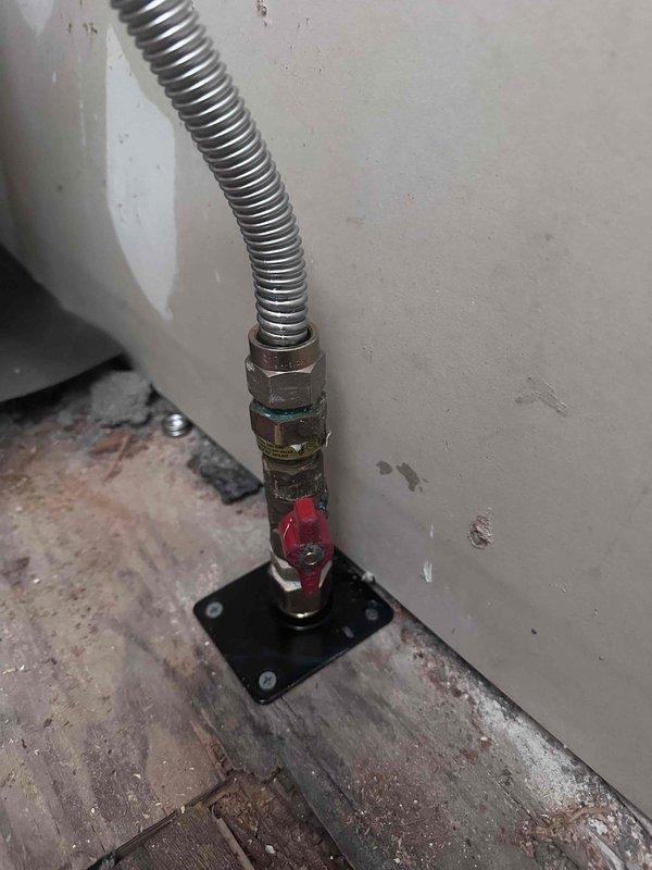 Relocated gas supply line to accommodate appliance repositioning. Installed new flexible gas connector with shutoff valve and floor-mounted brass fitting secured to concrete base. Routed metallic conduit from floor connection point to appliance inlet, ensuring proper clearances and code-compliant installation. Completed work in area with existing flooring damage and wall modifications from previous renovations. Relocated gas supply line to accommodate appliance repositioning. Installed new flexible gas connector with shutoff valve and floor-mounted brass fitting secured to concrete base. Routed metallic conduit from floor connection point to appliance inlet, ensuring proper clearances and code-compliant installation. Completed work in area with existing flooring damage and wall modifications from previous renovations.