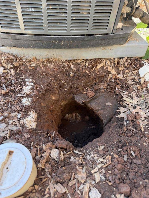 Excavated and exposed underground copper piping system for inspection and repair access. Documented existing plumbing infrastructure including oxidized copper pipe with branch connections and adjacent concrete utility components positioned near HVAC equipment foundation. Completed trenching work and site photography for service records. Excavated and exposed underground copper piping system for inspection and repair access. Documented existing plumbing infrastructure including oxidized copper pipe with branch connections and adjacent concrete utility components positioned near HVAC equipment foundation. Completed trenching work and site photography for service records.