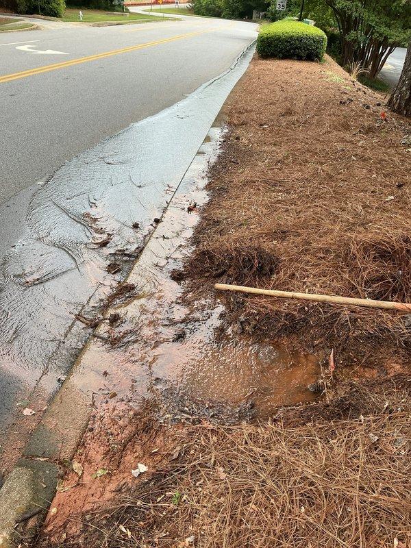 Responded to water leak investigation at residential property where water pooling was observed approximately one foot from street curb. County utilities confirmed leak was located on customer's private side of service line. Upon arrival, documented extensive water damage with muddy runoff flowing from landscaped area across concrete curb onto asphalt roadway, creating brown sediment trails and standing water. Visual inspection revealed active water intrusion causing soil erosion in mulched landscape bed adjacent to sidewalk, with reddish-brown clay-rich sediment dispersing across hardscaped surfaces and into street. Photographed conditions showing water migration pattern from property landscape through curb area. No further action taken at this time pending customer decision on repair options for private-side water line leak. Responded to water leak investigation at residential property where water pooling was observed approximately one foot from street curb. County utilities confirmed leak was located on customer's private side of service line. Upon arrival, documented extensive water damage with muddy runoff flowing from landscaped area across concrete curb onto asphalt roadway, creating brown sediment trails and standing water. Visual inspection revealed active water intrusion causing soil erosion in mulched landscape bed adjacent to sidewalk, with reddish-brown clay-rich sediment dispersing across hardscaped surfaces and into street. Photographed conditions showing water migration pattern from property landscape through curb area. No further action taken at this time pending customer decision on repair options for private-side water line leak.