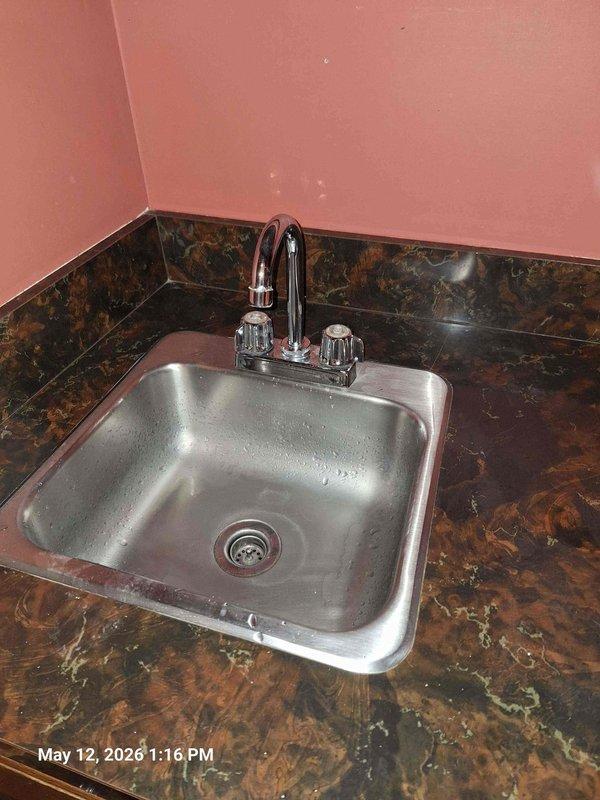 Completed real estate inspection per home inspection report requirements. Inspected and photographed kitchen sink installation, verifying proper mounting of stainless steel basin in countertop with functional faucet assembly. Examined bathroom vanity plumbing beneath sink, documenting supply line conditions and connections to faucet fixtures. Noted aging visible on supply line fittings. Sump pump inspection could not be completed or was not accessible during visit. All accessible plumbing fixtures photographed for documentation purposes. Completed real estate inspection per home inspection report requirements. Inspected and photographed kitchen sink installation, verifying proper mounting of stainless steel basin in countertop with functional faucet assembly. Examined bathroom vanity plumbing beneath sink, documenting supply line conditions and connections to faucet fixtures. Noted aging visible on supply line fittings. Sump pump inspection could not be completed or was not accessible during visit. All accessible plumbing fixtures photographed for documentation purposes.