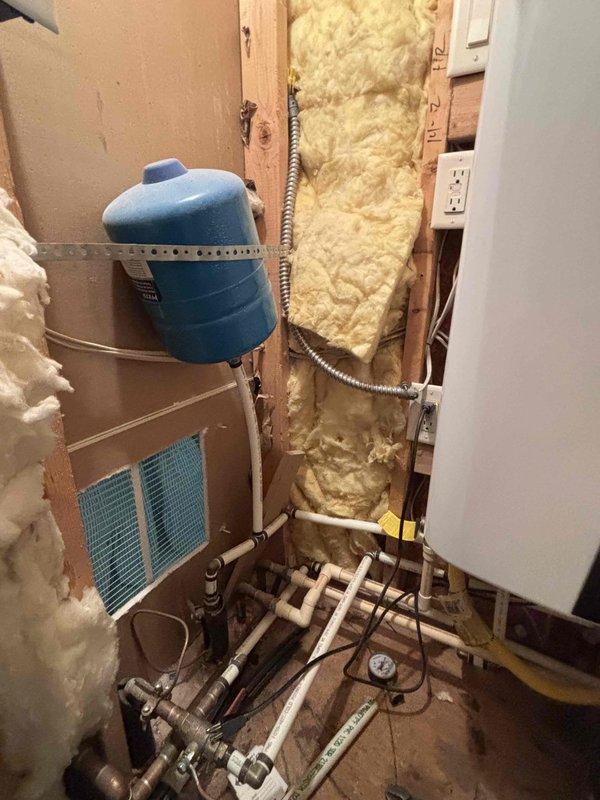 Responded to service call for tankless water heater with reported leak from connected piping and non-functional recirculation pump. Upon arrival, inspected mechanical room installation including expansion tank, pressure regulation system, and PVC/copper piping network. Located leak source at pipe connection point near tankless unit. Diagnosed recirculation pump failure preventing hot water circulation throughout system. Verified system pressure readings via installed gauge to ensure proper operating parameters. Assessed complete plumbing configuration including multiple pipe runs, fittings, and control components within exposed wall cavity installation. Documented existing conditions through photography showing expansion tank mounting, pressure monitoring equipment, and complex piping arrangement with various connections and valves. Responded to service call for tankless water heater with reported leak from connected piping and non-functional recirculation pump. Upon arrival, inspected mechanical room installation including expansion tank, pressure regulation system, and PVC/copper piping network. Located leak source at pipe connection point near tankless unit. Diagnosed recirculation pump failure preventing hot water circulation throughout system. Verified system pressure readings via installed gauge to ensure proper operating parameters. Assessed complete plumbing configuration including multiple pipe runs, fittings, and control components within exposed wall cavity installation. Documented existing conditions through photography showing expansion tank mounting, pressure monitoring equipment, and complex piping arrangement with various connections and valves.