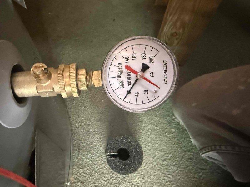 Continued inspection of residential plumbing system with focus on water pressure regulation and supply line components. Accessed attic space to examine and photograph pressure regulator valve assembly mounted on copper supply line, including associated shutoff valves and brass fittings. Verified pressure gauge readings and documented current system pressure status, noting gauge indicating near-zero pressure reading on 0-200 PSI scale. Inspected condition of copper piping, PVC drain lines, and electrical wiring routed through ceiling space. Assessment included visual examination of valve operation, connection integrity, and overall system configuration for compliance with plumbing standards. Continued inspection of residential plumbing system with focus on water pressure regulation and supply line components. Accessed attic space to examine and photograph pressure regulator valve assembly mounted on copper supply line, including associated shutoff valves and brass fittings. Verified pressure gauge readings and documented current system pressure status, noting gauge indicating near-zero pressure reading on 0-200 PSI scale. Inspected condition of copper piping, PVC drain lines, and electrical wiring routed through ceiling space. Assessment included visual examination of valve operation, connection integrity, and overall system configuration for compliance with plumbing standards.