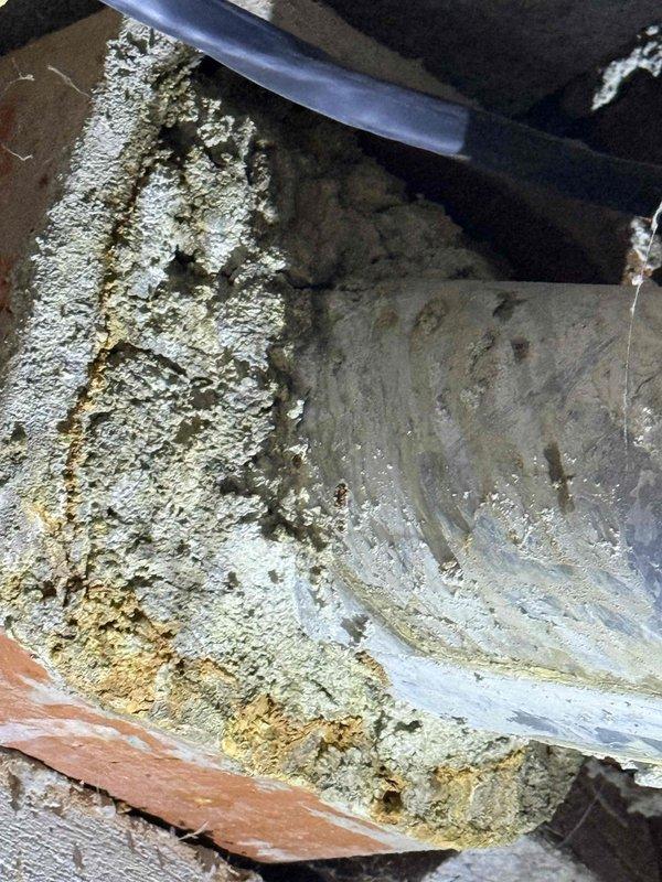 Responded to customer complaint of gas or burning odor near water heater. Performed thorough inspection of water heater and surrounding plumbing components. Examined copper supply lines, brass fittings, and galvanized flue vent pipe for signs of gas leaks or combustion issues. Documented heavily corroded and deteriorated flue vent system with significant mineral buildup and corrosion on metal surfaces. Identified crusty white and yellowish deposits indicating potential exhaust condensation issues and compromised venting. Photographed installation showing aged galvanized flue pipe with visible weathering and HVAC components with substantial mineral accumulation. Recommended immediate evaluation of venting system due to corrosion severity and potential safety concerns related to improper exhaust ventilation.