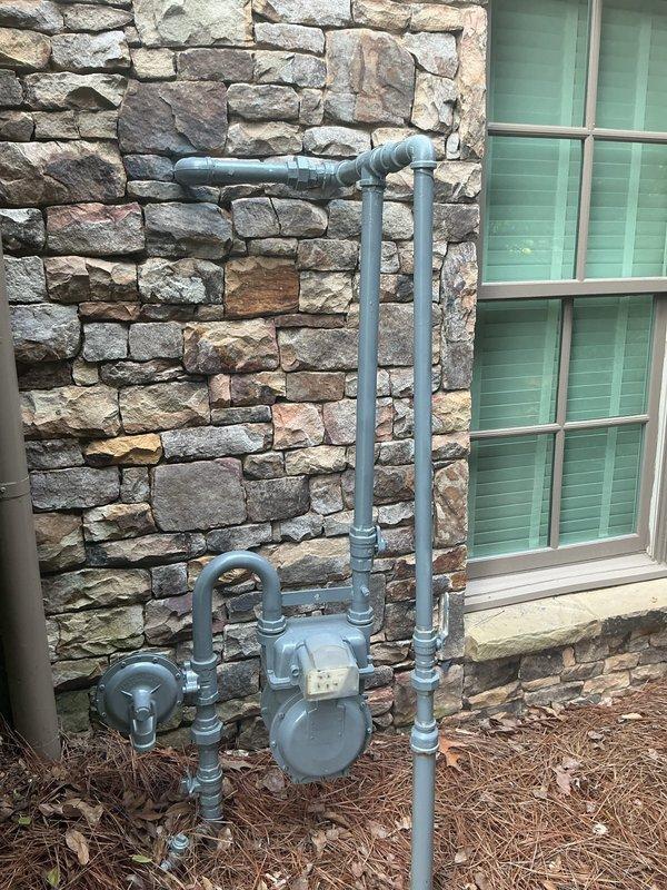 Completed comprehensive assessment of existing residential gas meter system for conversion from low-pressure to high-pressure configuration. Evaluated current exterior-mounted gas meter assembly with blue-gray painted piping, including vertical and horizontal runs with multiple elbow joints and connections positioned against decorative stone exterior wall. Documented existing round dial meter, circular valve control, and complete piping configuration to determine scope of regulator replacement and system upgrade requirements. Assessed secondary PVC conduit installation with T-junction fitting and vertical runs near gas system. Provided detailed photographic documentation of current installation for regulatory compliance and system planning purposes.