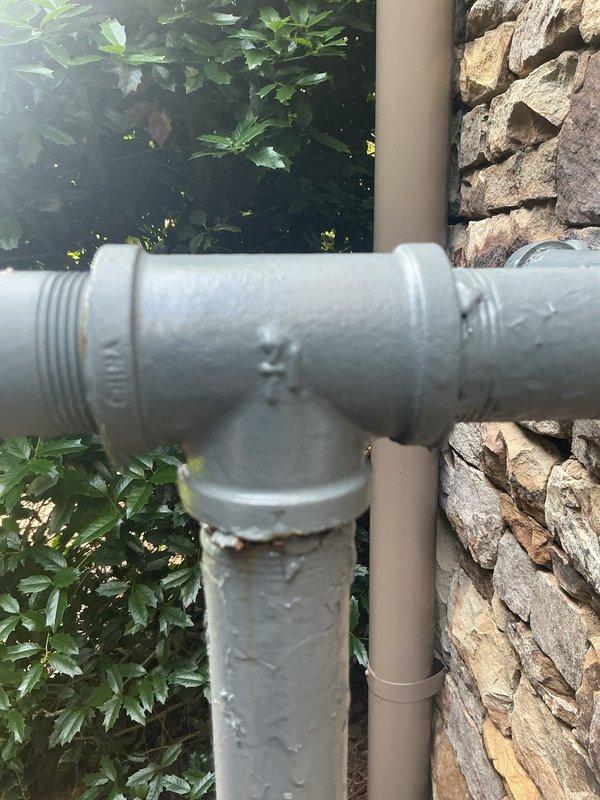 Completed comprehensive assessment of existing residential gas meter system for conversion from low-pressure to high-pressure configuration. Evaluated current exterior-mounted gas meter assembly with blue-gray painted piping, including vertical and horizontal runs with multiple elbow joints and connections positioned against decorative stone exterior wall. Documented existing round dial meter, circular valve control, and complete piping configuration to determine scope of regulator replacement and system upgrade requirements. Assessed secondary PVC conduit installation with T-junction fitting and vertical runs near gas system. Provided detailed photographic documentation of current installation for regulatory compliance and system planning purposes.