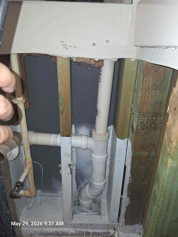Responded to water leak behind wall where remediation crew had already begun opening drywall. Accessed exposed wall cavity to inspect plumbing system and assess source of moisture intrusion. Documented conditions showing water-damaged wooden studs with visible green discoloration and moisture staining on vertical framing members. Inspected white PVC drainage and vent piping running vertically through cavity, including multiple joints, fittings, and connections. Examined plumbing components and shut-off valve assembly for signs of failure or leakage. Photographed damaged areas and plumbing configuration for documentation purposes. Confirmed extent of water damage to structural framing and identified affected plumbing chase area.