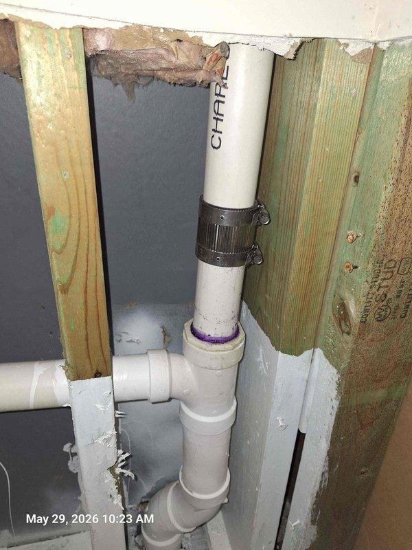 Responded to water leak behind wall where remediation crew had already begun opening drywall. Accessed exposed wall cavity to inspect plumbing system and assess source of moisture intrusion. Documented conditions showing water-damaged wooden studs with visible green discoloration and moisture staining on vertical framing members. Inspected white PVC drainage and vent piping running vertically through cavity, including multiple joints, fittings, and connections. Examined plumbing components and shut-off valve assembly for signs of failure or leakage. Photographed damaged areas and plumbing configuration for documentation purposes. Confirmed extent of water damage to structural framing and identified affected plumbing chase area.