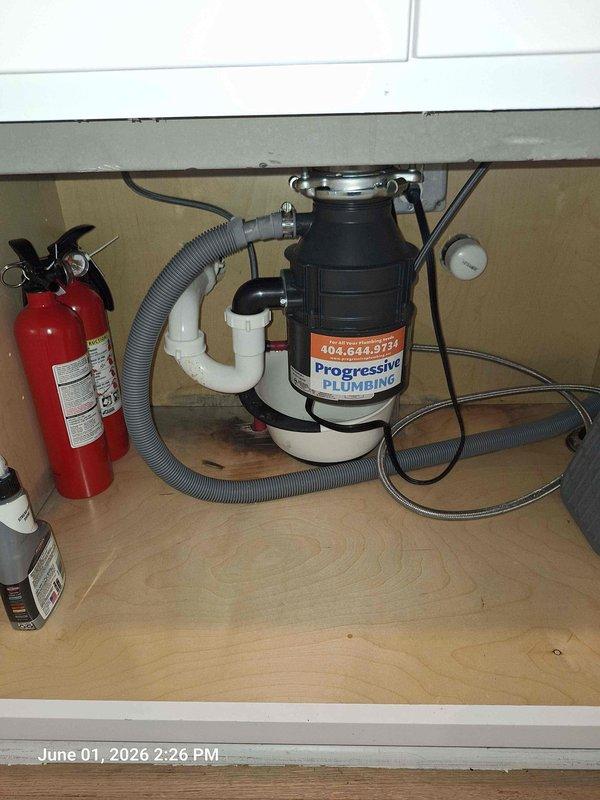 Responded to kitchen sink leak complaint. Upon inspection, identified leak originating from garbage disposal unit and associated drain connections beneath sink. Examined all plumbing components including black garbage disposal unit, white PVC P-trap assembly, and connection points. Checked system pressure using gauge to verify proper operation and rule out pressure-related issues. Tightened disposal mounting assembly and drain fittings to eliminate leak source. Tested system under running water conditions to confirm repair integrity and verify no additional moisture present.