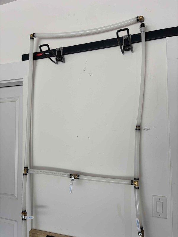 Installed iSpring water filtration system and booster pump assembly with wall-mounted frame and pressure regulation components. Connected white PVC supply lines with brass compression fittings and pressure relief valve, secured all components to wall with mounting brackets, and verified proper system operation.