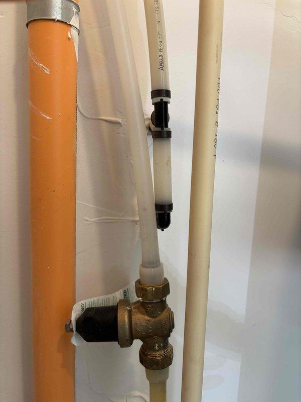 Installed iSpring water filtration system and booster pump assembly with wall-mounted frame and pressure regulation components. Connected white PVC supply lines with brass compression fittings and pressure relief valve, secured all components to wall with mounting brackets, and verified proper system operation.