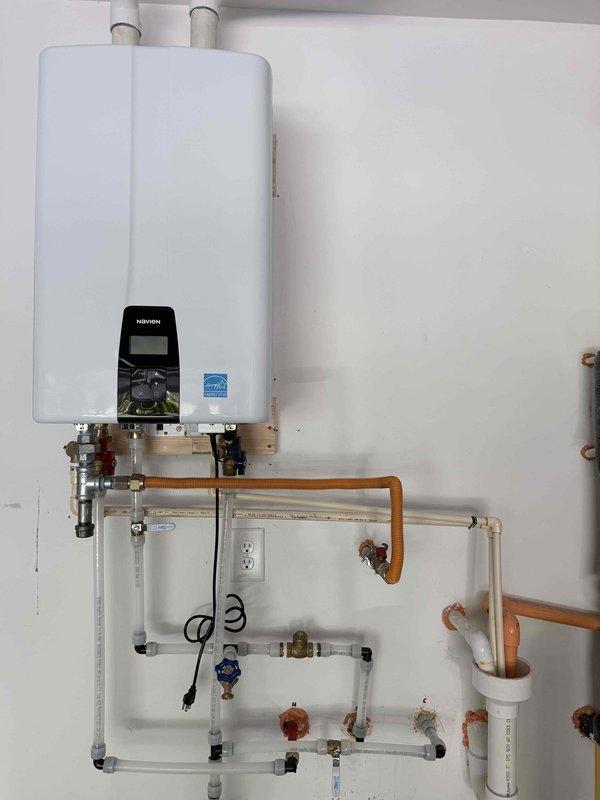 Completed tankless water heater replacement with full plumbing integration. Removed existing unit and installed new wall-mounted tankless water heater with digital display and control panel. Configured complete piping system including copper supply lines, white PVC drainage, and multiple shut-off valves with isolation capabilities at key connection points. Installed brass fittings and pressure relief valves throughout the system for proper operation and safety compliance. Established electrical connections with dedicated outlet placement and proper cord management. Verified all connections for leaks, tested system operation, and confirmed proper water flow and temperature control functionality.