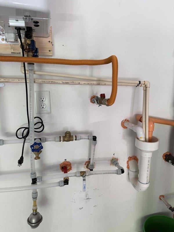 Completed tankless water heater replacement with full plumbing integration. Removed existing unit and installed new wall-mounted tankless water heater with digital display and control panel. Configured complete piping system including copper supply lines, white PVC drainage, and multiple shut-off valves with isolation capabilities at key connection points. Installed brass fittings and pressure relief valves throughout the system for proper operation and safety compliance. Established electrical connections with dedicated outlet placement and proper cord management. Verified all connections for leaks, tested system operation, and confirmed proper water flow and temperature control functionality.