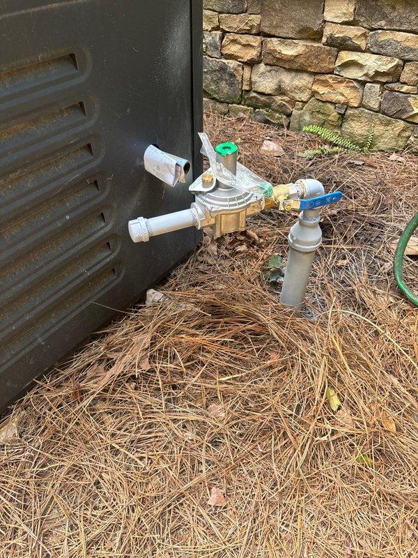 Installed new gas pressure regulator assembly with associated brass fittings and multi-diameter PVC piping configuration against exterior stone wall foundation. Coordinated with AGL utility company for on-site gas service connection and system pressurization, completing installation to code specifications with green-handled shutoff valve for system control.