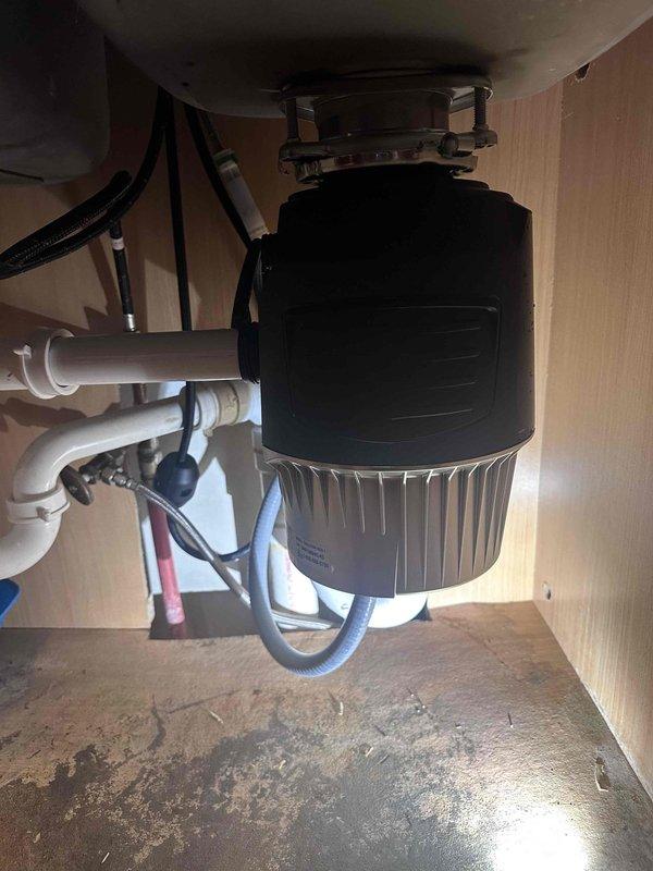Responded to service call for leaking garbage disposal unit. Upon inspection, identified active leak from disposal housing and deteriorated mounting assembly. Documented existing water damage to cabinet floor and compromised plumbing connections. Photographed disposal unit, drain assembly, and affected areas for service records. Assessed condition of mounting flange, drain connections, and PVC trap configuration to determine repair requirements.