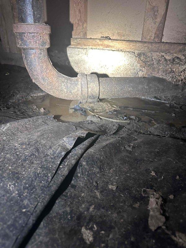 Responded to sewage leak in crawlspace and conducted thorough inspection of affected area. Upon arrival, accessed crawlspace and located corroded metal drain pipe with active leak contaminating the space. Documented existing conditions including severely deteriorated P-trap assembly with extensive rust and oxidation compromising pipe integrity. Photographed damaged plumbing components, contaminated soil beneath leak point, and surrounding structural elements for record purposes. Assessed crawlspace environment noting accumulated debris, dust-covered flooring, and exposed insulation materials in vicinity of leak. Identified compromised drainage system requiring replacement of corroded pipe section to resolve sewage discharge issue and prevent further contamination of crawlspace area.