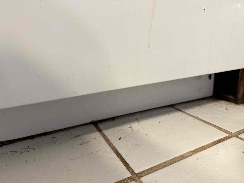 Responded to water leak behind stove. Upon inspection, found water damage and debris accumulation on flooring in corner area where appliance meets wall. Identified source of leak, performed necessary repairs to stop water intrusion. Cleaned affected area and documented existing conditions including staining on floor tiles, wall discoloration, and baseboard damage. Verified leak was resolved and area was properly dried to prevent further water damage or mold growth.